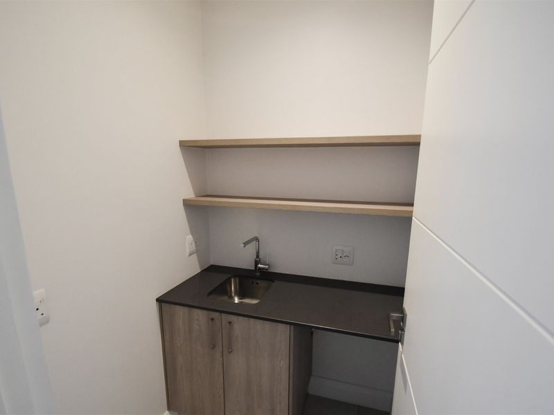 A compact, modern scullery or utility area featuring built-in cabinetry, a stainless steel sink, stone countertop, and floating shelving.
