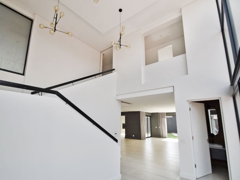 Spacious double-volume entrance hall featuring a modern staircase with black metal handrails, tiled flooring, and contemporary pendant lighting.