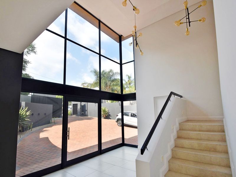Spacious double-volume entrance hall featuring floor-to-ceiling windows, modern pendant lighting, and a staircase with a sleek black handrail.