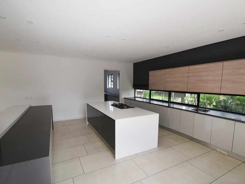 Modern, spacious kitchen featuring a central island with a built-in cooktop, sleek cabinetry, and large windows overlooking the garden.