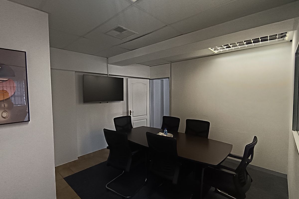 A functional office meeting room featuring recessed ceiling lighting, air conditioning, and a wall-mounted television screen.