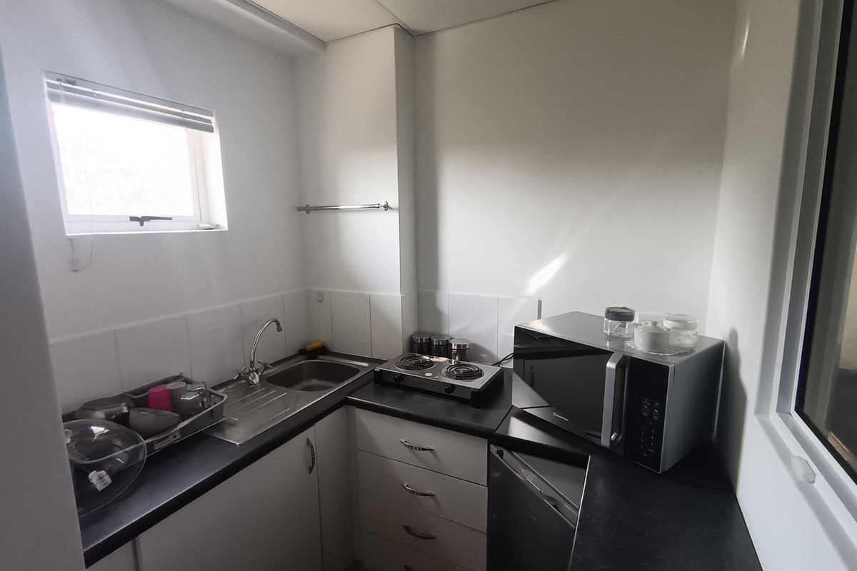 A compact office kitchenette featuring built-in cabinetry, a stainless steel sink, tiled backsplash, and laminate countertops.