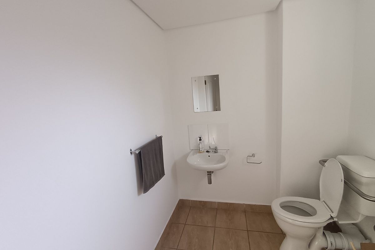 A functional office bathroom featuring a wall-mounted basin, standard toilet, and tiled flooring with neutral white walls.