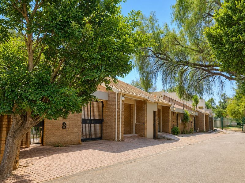 Street-level view of the townhouse complex featuring a brick facade, tiled roof, and paved driveway entrance.