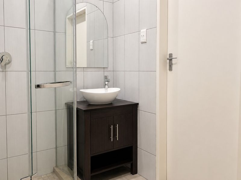 A modern bathroom featuring a glass shower enclosure, a dark wood vanity with a vessel sink, and neutral wall tiling.