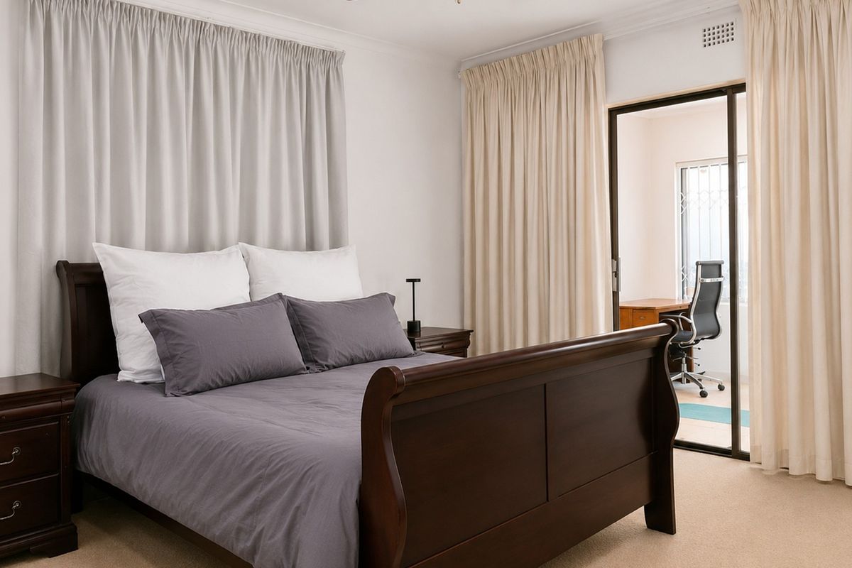 A well-maintained bedroom featuring neutral carpeting, ceiling cornicing, and a sliding glass door providing access to an adjoining office space.