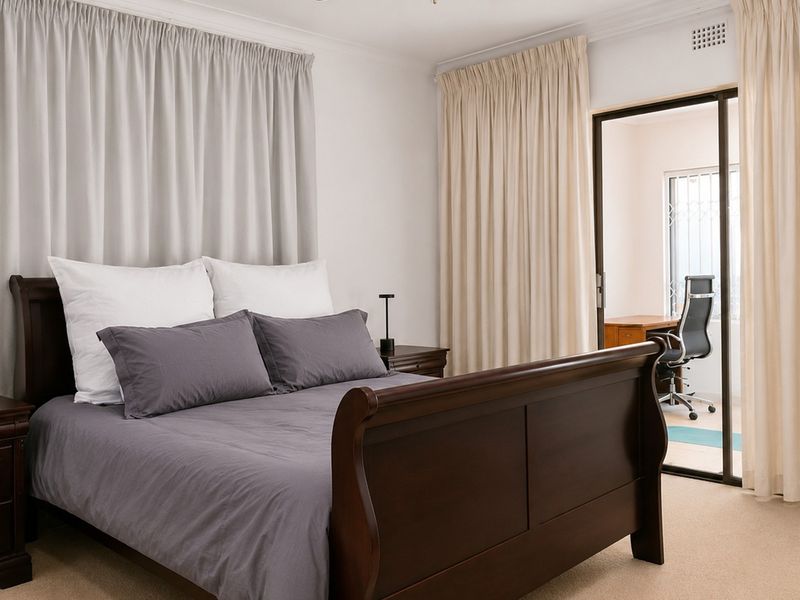 A well-maintained bedroom featuring neutral carpeting, ceiling cornicing, and a sliding glass door providing access to an adjoining office space.