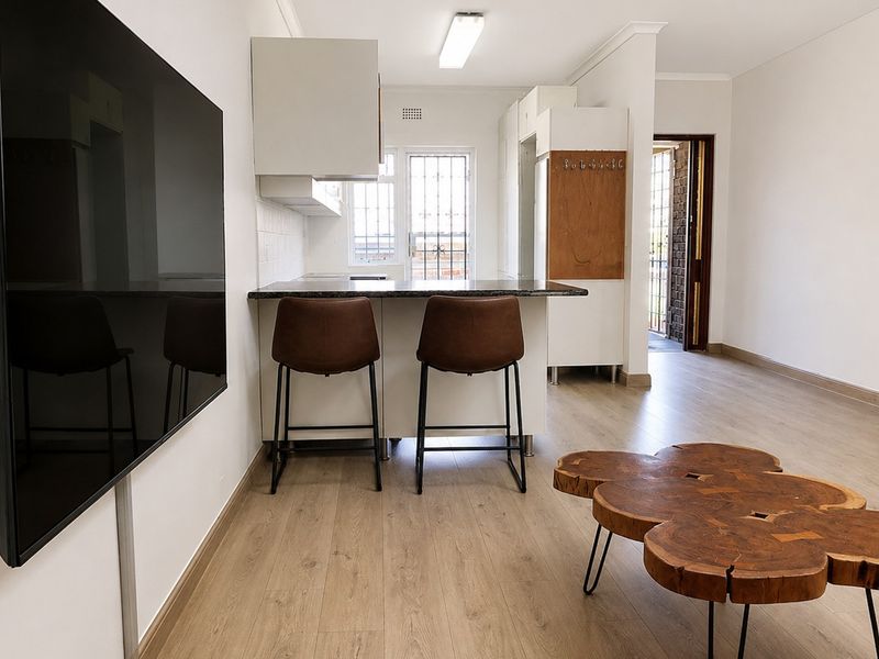 Open-plan living area featuring laminate flooring, a compact kitchen with granite countertops, and direct access to the exterior through a security gate.