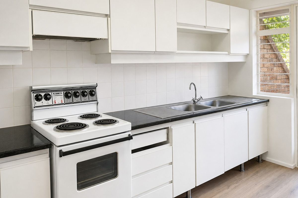 A clean, functional kitchen featuring white cabinetry, black countertops, a double sink, and a freestanding electric stove with an integrated extractor fan.