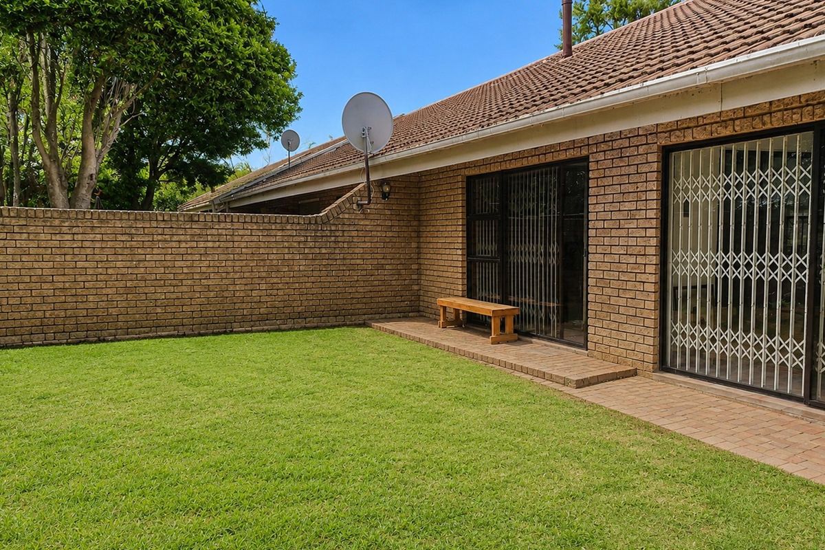 A private rear garden featuring a paved patio area, brick boundary wall, and sliding glass doors with security gates leading into the townhouse.