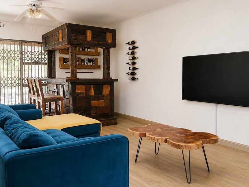 A comfortable living room featuring a custom built-in wooden bar, laminate flooring, and a ceiling fan, with direct access to an outdoor area.