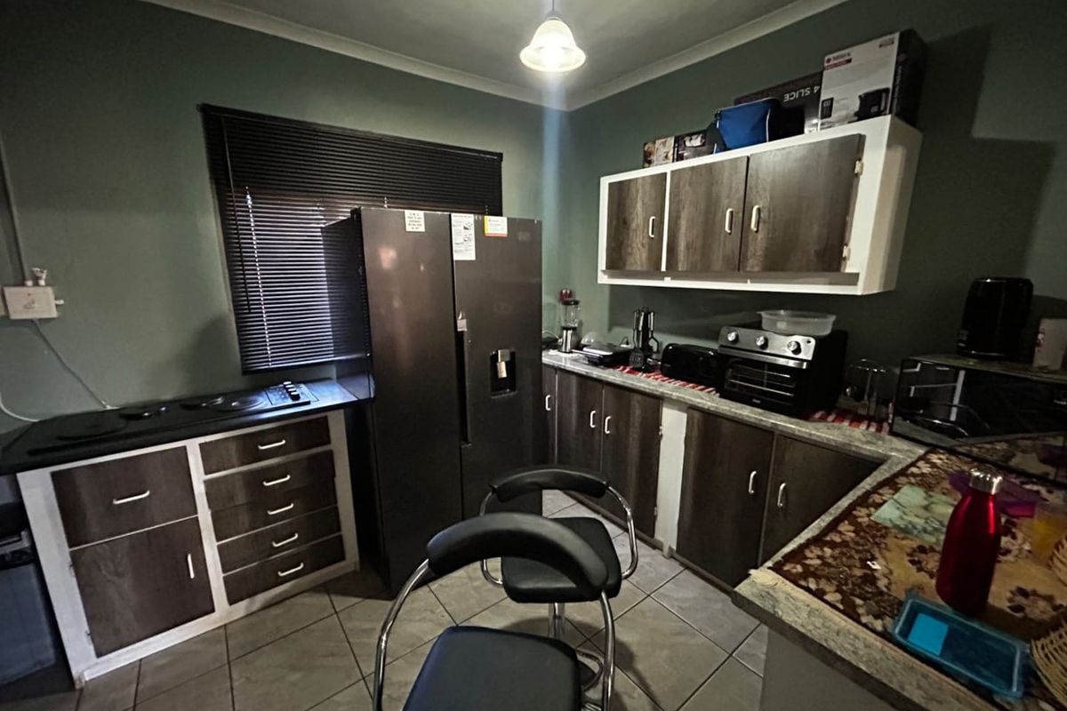 A functional kitchen featuring dark wood-look cabinetry, tiled flooring, and an integrated electric hob, offering a practical layout with ample storage space.