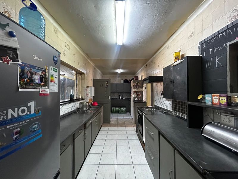 A functional galley-style kitchen featuring dark cabinetry, laminate countertops, gas hob, extractor fan, and tiled finishes throughout.