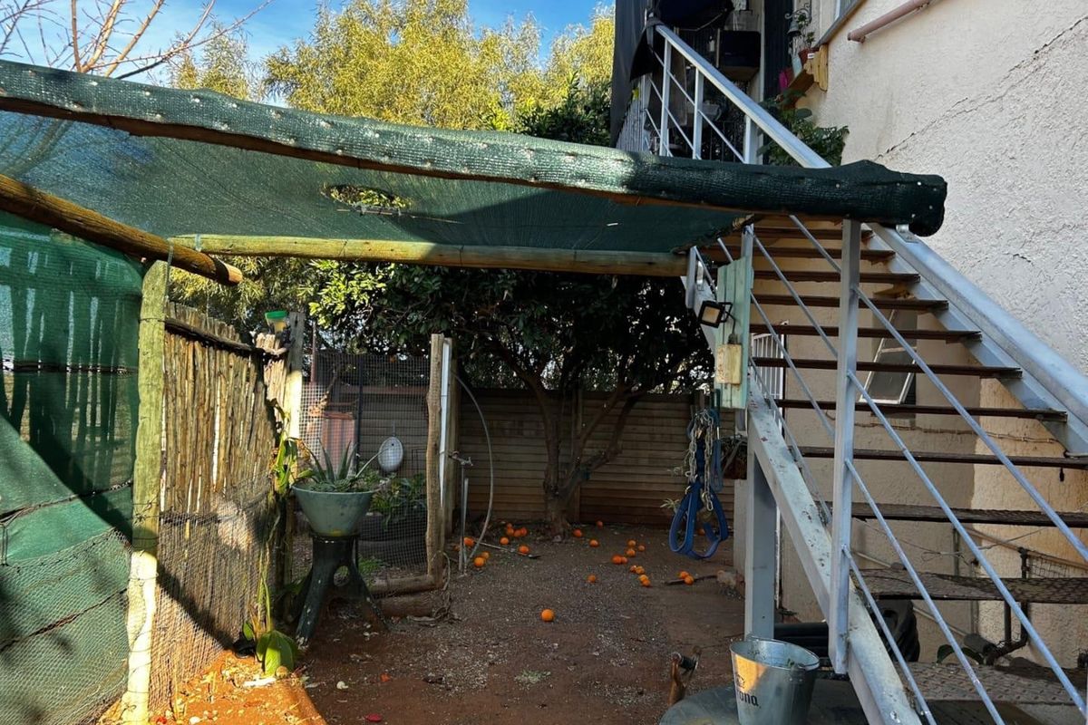 Rear outdoor area featuring an external metal staircase, shade cloth canopy, and perimeter fencing, requiring maintenance and landscaping improvements.