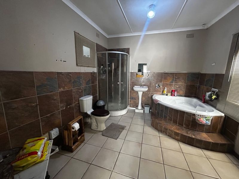 A spacious bathroom featuring a corner bathtub, separate shower enclosure, pedestal basin, and tiled finishes throughout, offering potential for modernization.