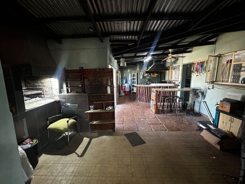Covered outdoor entertainment area featuring a built-in braai, tiled flooring, and a rustic bar counter under an exposed beam roof structure.
