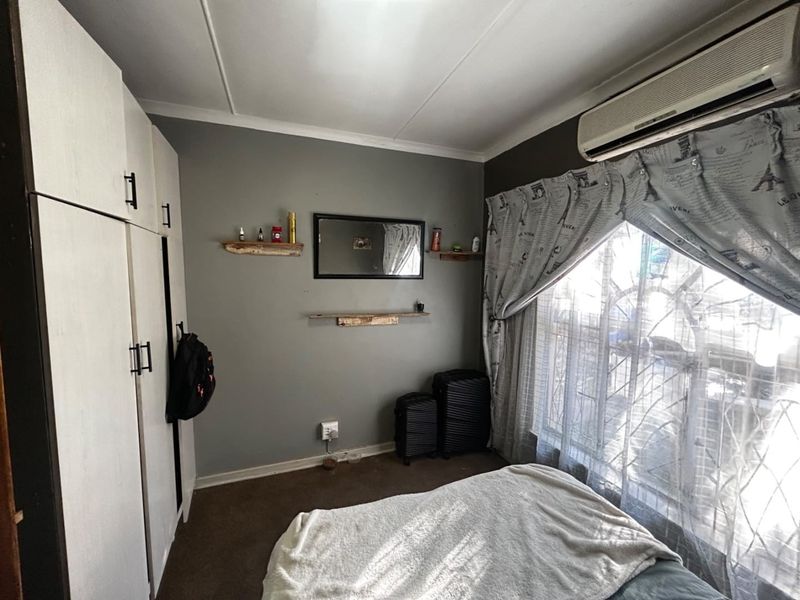 A bedroom featuring built-in cupboards, a split-system air conditioner, and security bars on the window.