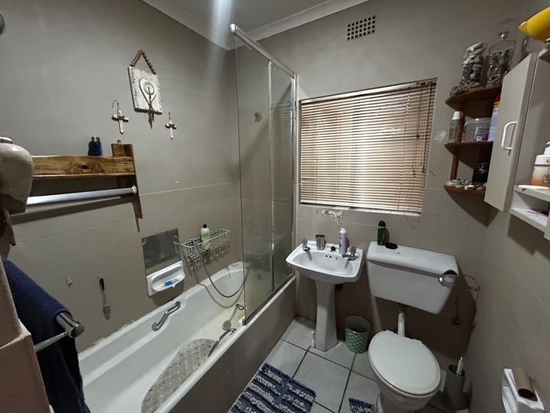 A functional bathroom featuring a pedestal basin, toilet, and a bathtub with a glass shower screen, finished with tiled walls and flooring.