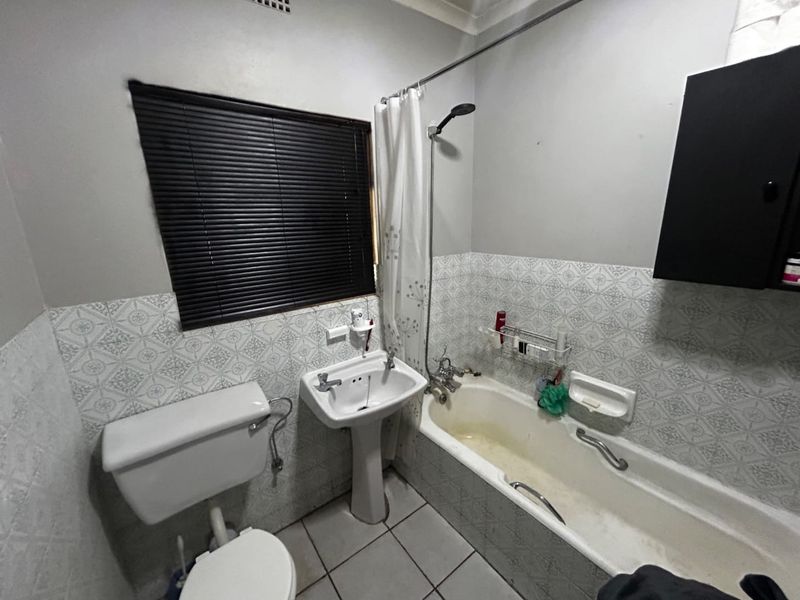 A functional bathroom featuring a pedestal basin, bathtub with shower attachment, toilet, and patterned tiled splashbacks.