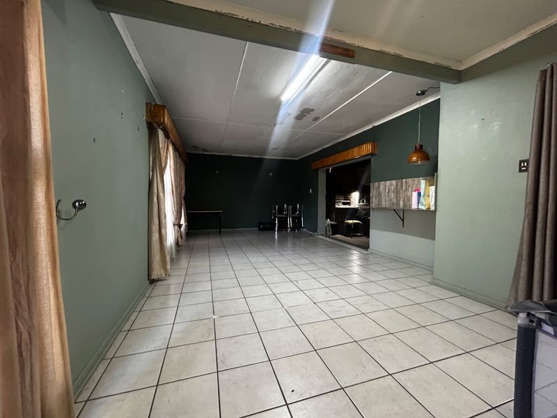 Spacious open-plan living area featuring tiled flooring, a built-in breakfast bar, and dual-tone wall finishes, ready for renovation and modernization.