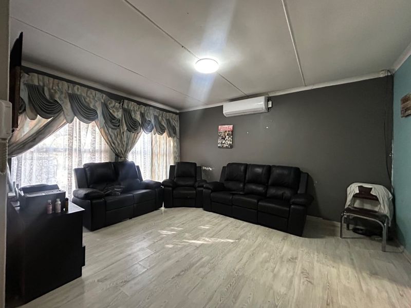 A living room featuring laminate flooring, a wall-mounted air conditioning unit, and neutral grey wall finishes.