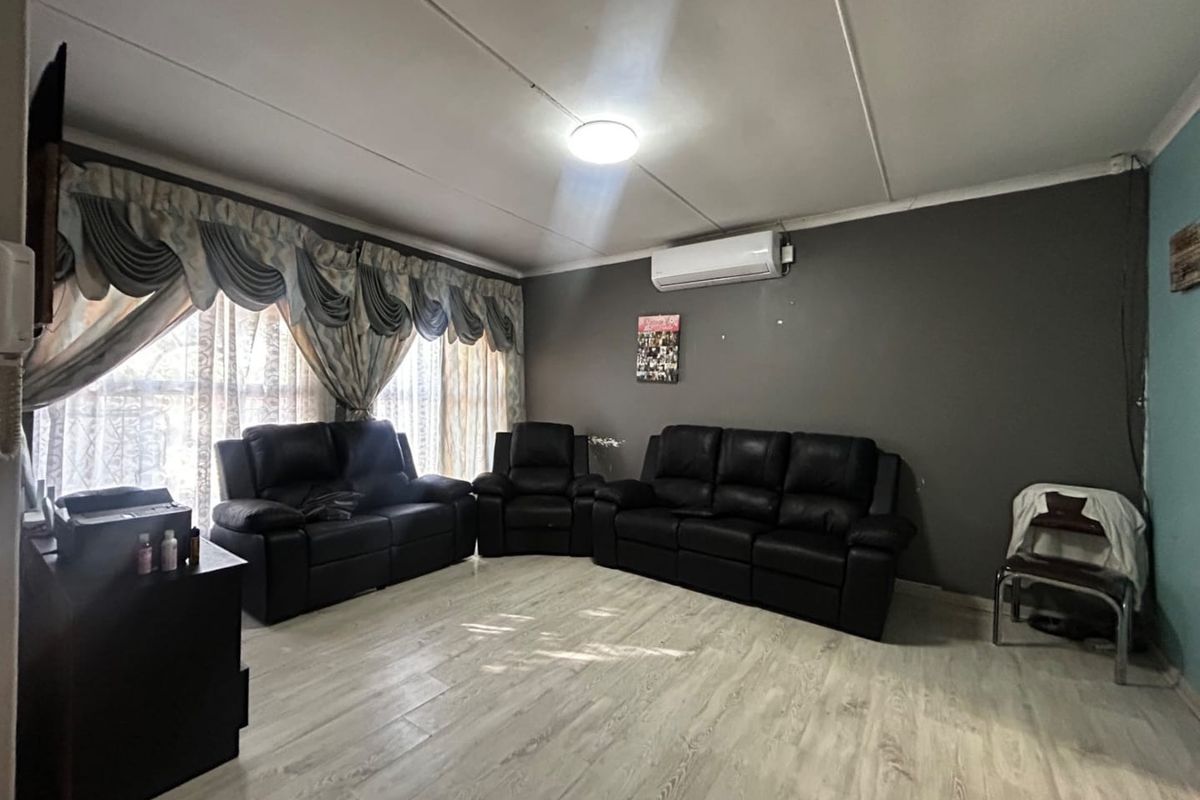 A living room featuring laminate flooring, a wall-mounted air conditioning unit, and neutral grey wall finishes.