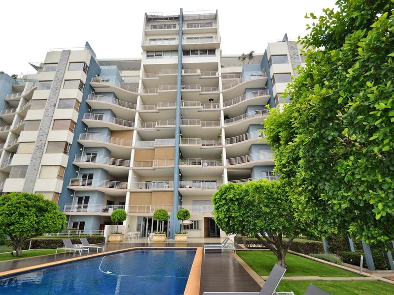 Rear view of a modern apartment complex featuring multiple balconies, a well-maintained swimming pool, and landscaped garden areas.