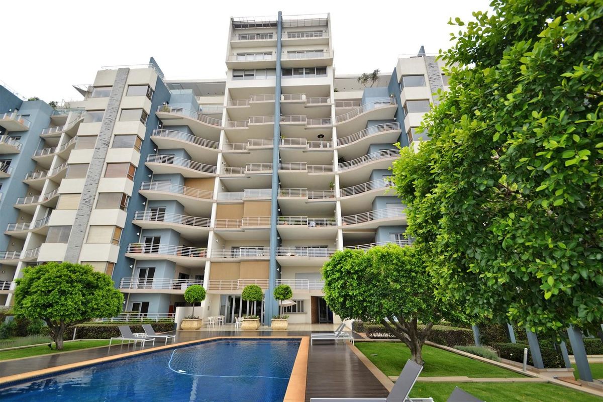 Rear view of a modern apartment complex featuring multiple balconies, a well-maintained swimming pool, and landscaped garden areas.