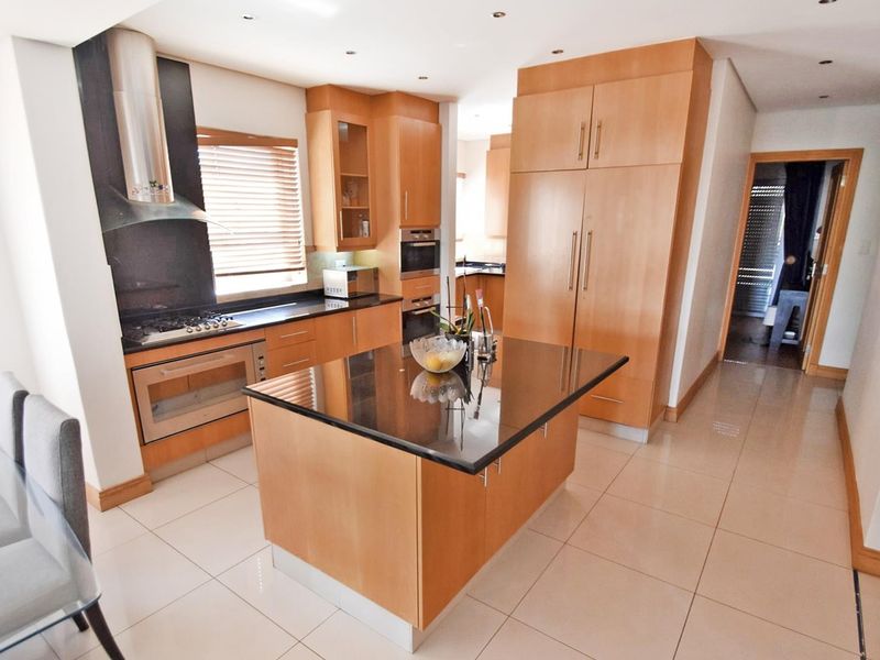 Modern kitchen featuring light wood cabinetry, granite countertops, a central island, and integrated stainless steel appliances with recessed lighting.