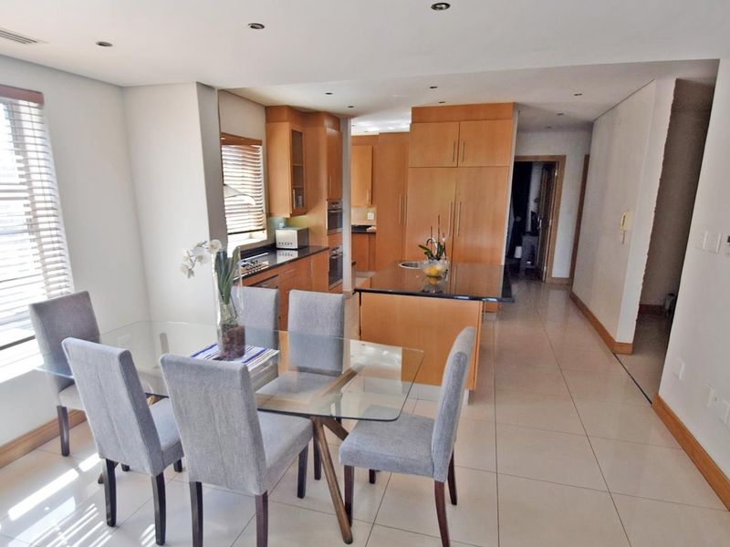 Open-plan kitchen and dining area featuring light wood cabinetry, granite countertops, a central island, and neutral tiled flooring throughout.