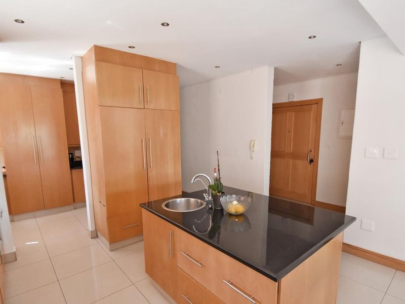 Modern kitchen featuring light wood cabinetry, a central island with a black granite countertop, undermount sink, and tiled flooring throughout.
