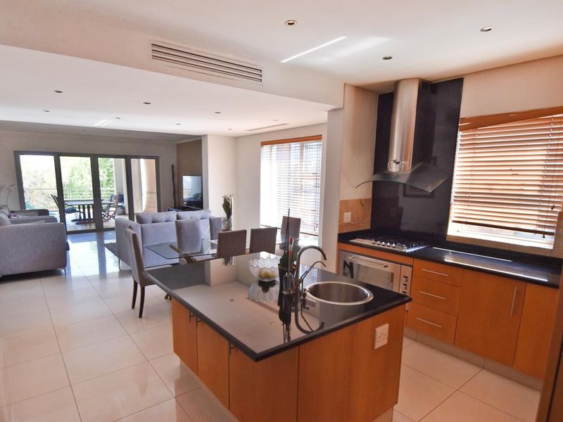 Spacious open-plan living area featuring a modern kitchen with granite countertops, gas hob, and seamless flow to the outdoor patio through sliding doors.