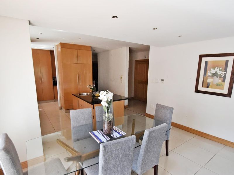Open plan living and dining area featuring a modern kitchen with built-in cabinetry, a central island with stone countertops, and neutral tiled flooring throughout.