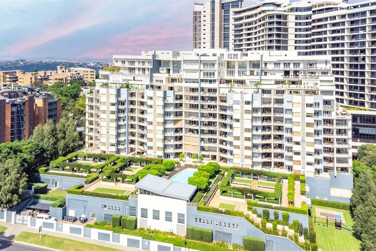 Aerial view of a modern apartment complex featuring landscaped gardens, a swimming pool, and multiple residential balconies.