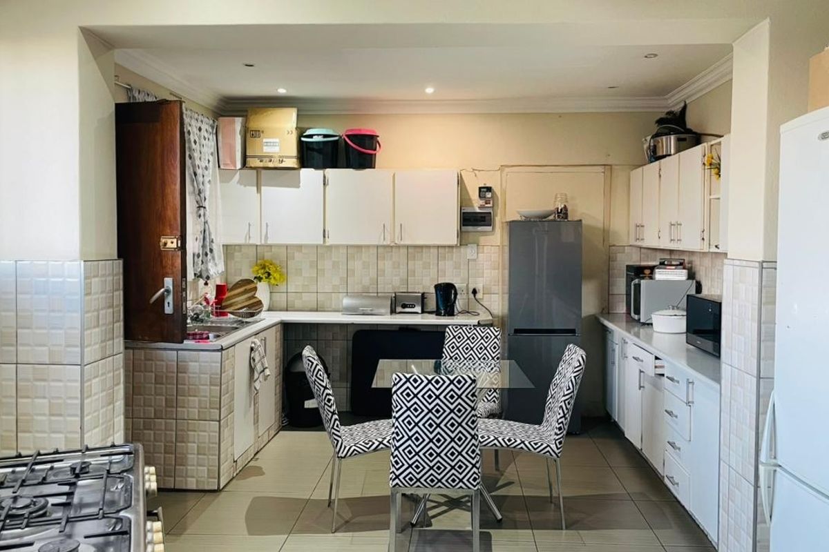 A functional kitchen featuring white built-in cabinetry, tiled backsplash, and tiled flooring, offering a practical layout with ample storage and workspace.