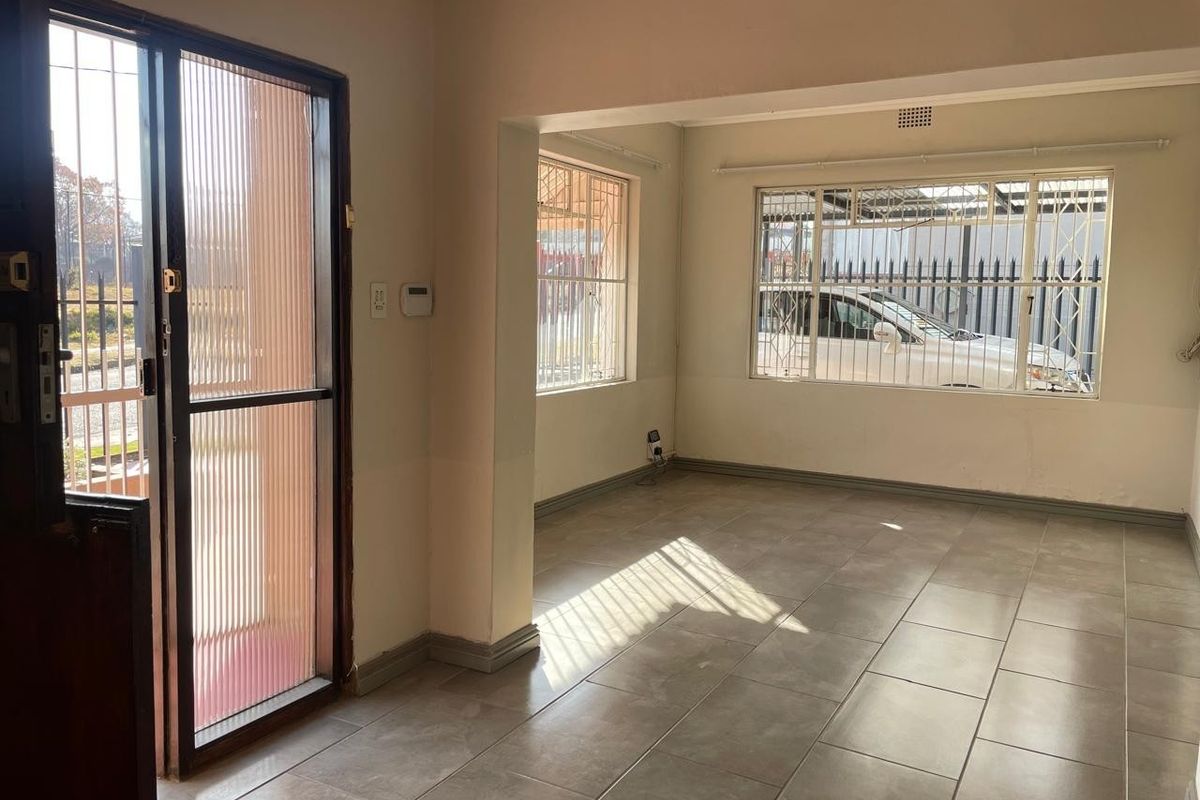 An empty, open-plan living area featuring neutral tiled flooring, security bars on windows, and a secure entrance door.