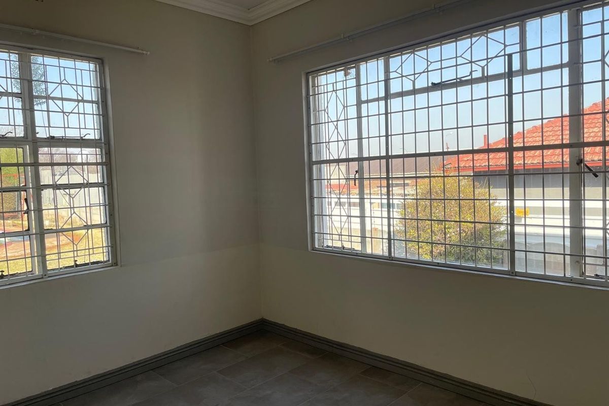 An empty bedroom featuring tiled flooring, large windows with security bars, and neutral wall finishes.