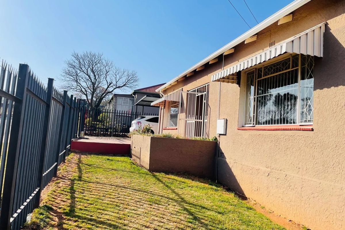 Rear exterior view of the property featuring a lawn area, metal security fencing, and window security bars with protective awnings.
