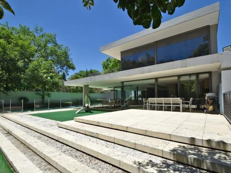 Modern rear exterior featuring a spacious stone patio, swimming pool with glass balustrade, and large sliding glass doors leading into the home.