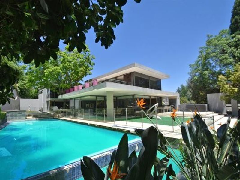 A modern multi-level residence featuring a large swimming pool, glass safety fencing, and expansive outdoor patio areas set within a landscaped garden.