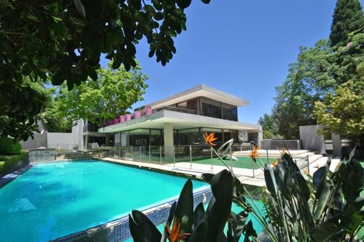 A modern multi-level residence featuring a large swimming pool, glass safety fencing, and expansive outdoor patio areas set within a landscaped garden.