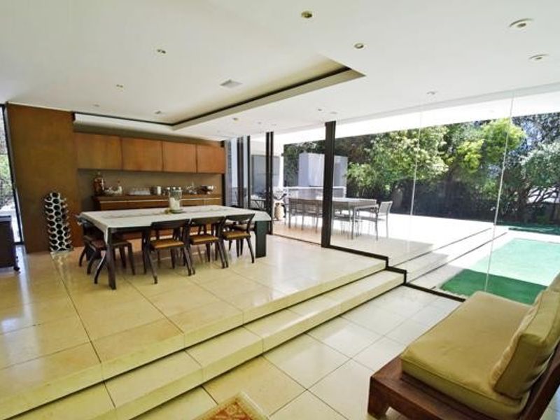 Spacious open-plan living and dining area featuring stone tile flooring, recessed lighting, and expansive glass sliding doors opening to an outdoor patio.