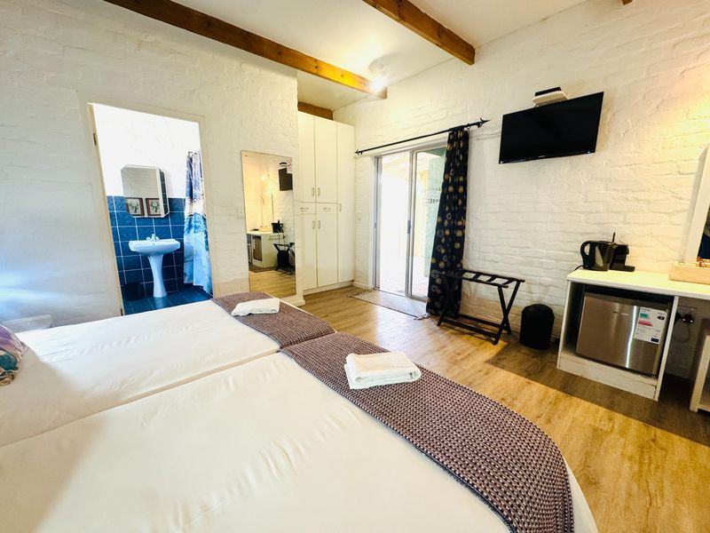 A bedroom featuring exposed timber ceiling beams, built-in wardrobe, and an en-suite bathroom with a pedestal basin, leading to an outdoor patio area.