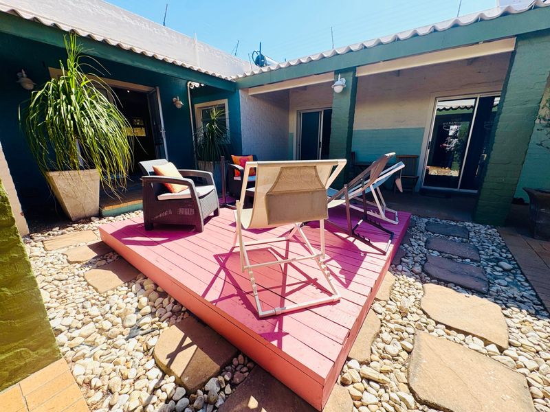 A covered outdoor patio area featuring a raised timber deck, stone paving, and direct access to the home through sliding glass doors.