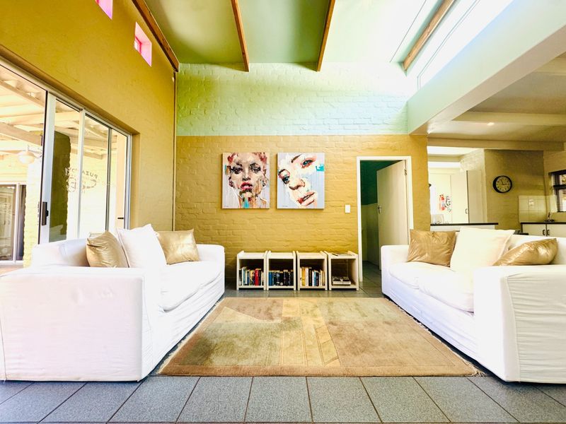 Spacious living room featuring exposed timber ceiling beams, clerestory windows for natural light, painted brick walls, and large sliding glass doors leading outdoors.