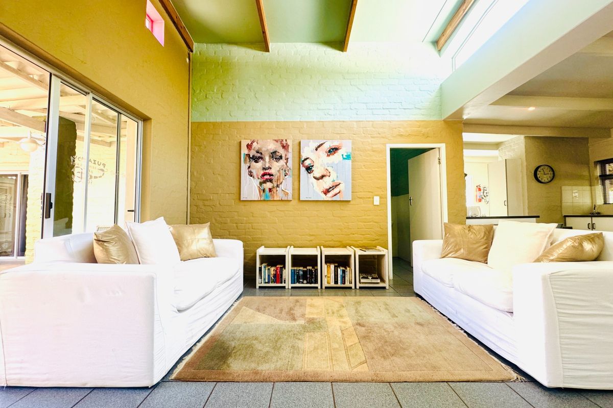 Spacious living room featuring exposed timber ceiling beams, clerestory windows for natural light, painted brick walls, and large sliding glass doors leading outdoors.