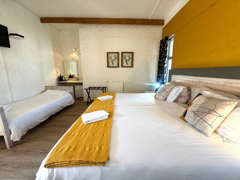 Spacious bedroom featuring exposed timber ceiling beams, painted brick walls, and a built-in vanity area.