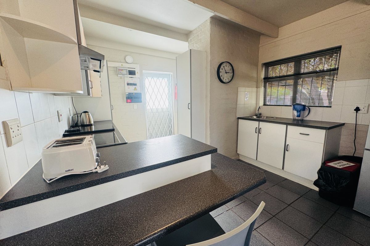 Functional kitchen featuring laminate countertops, built-in cabinetry, tiled flooring, and a security gate leading to the exterior.