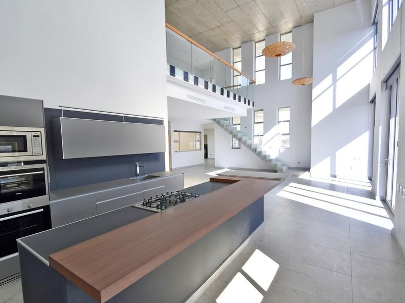 Spacious open-plan kitchen and living area featuring modern cabinetry, integrated appliances, a large island, and a striking double-volume ceiling with a mezzanine level.