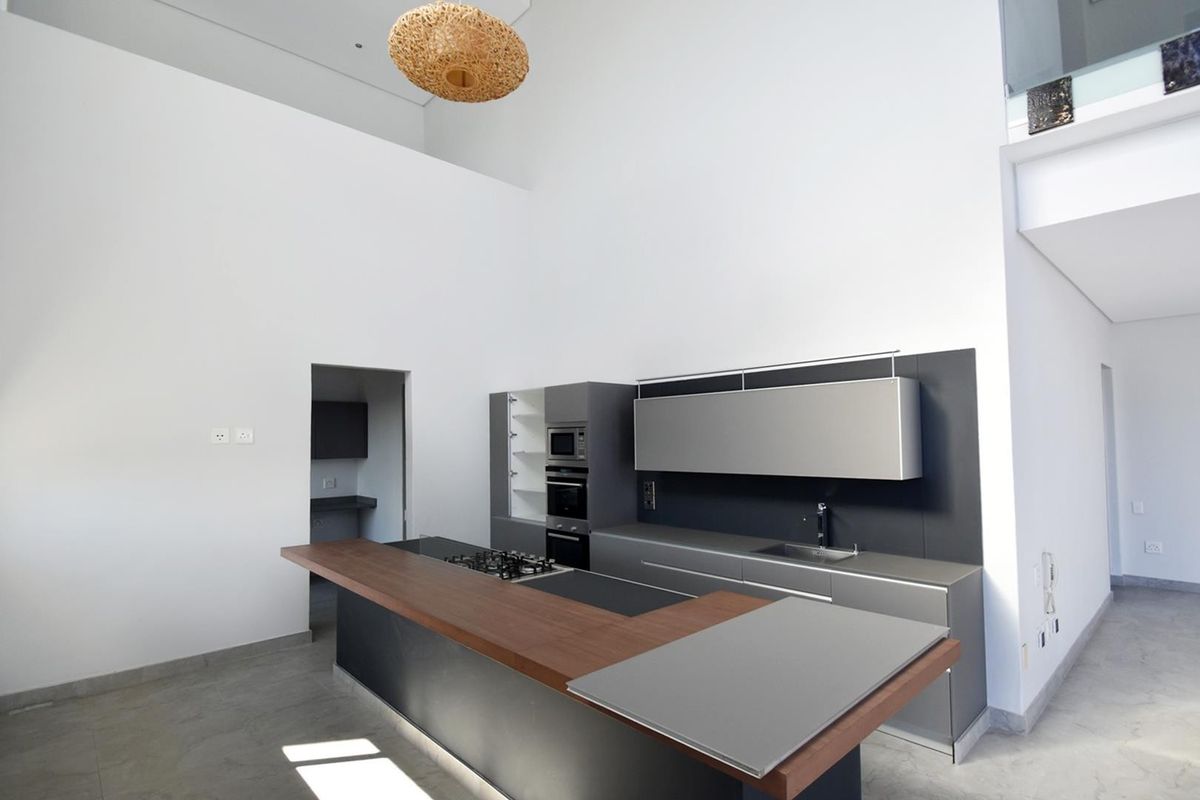 Modern kitchen featuring sleek dark cabinetry, integrated appliances, a spacious island with a wooden breakfast bar, and high ceilings in an open-plan layout.